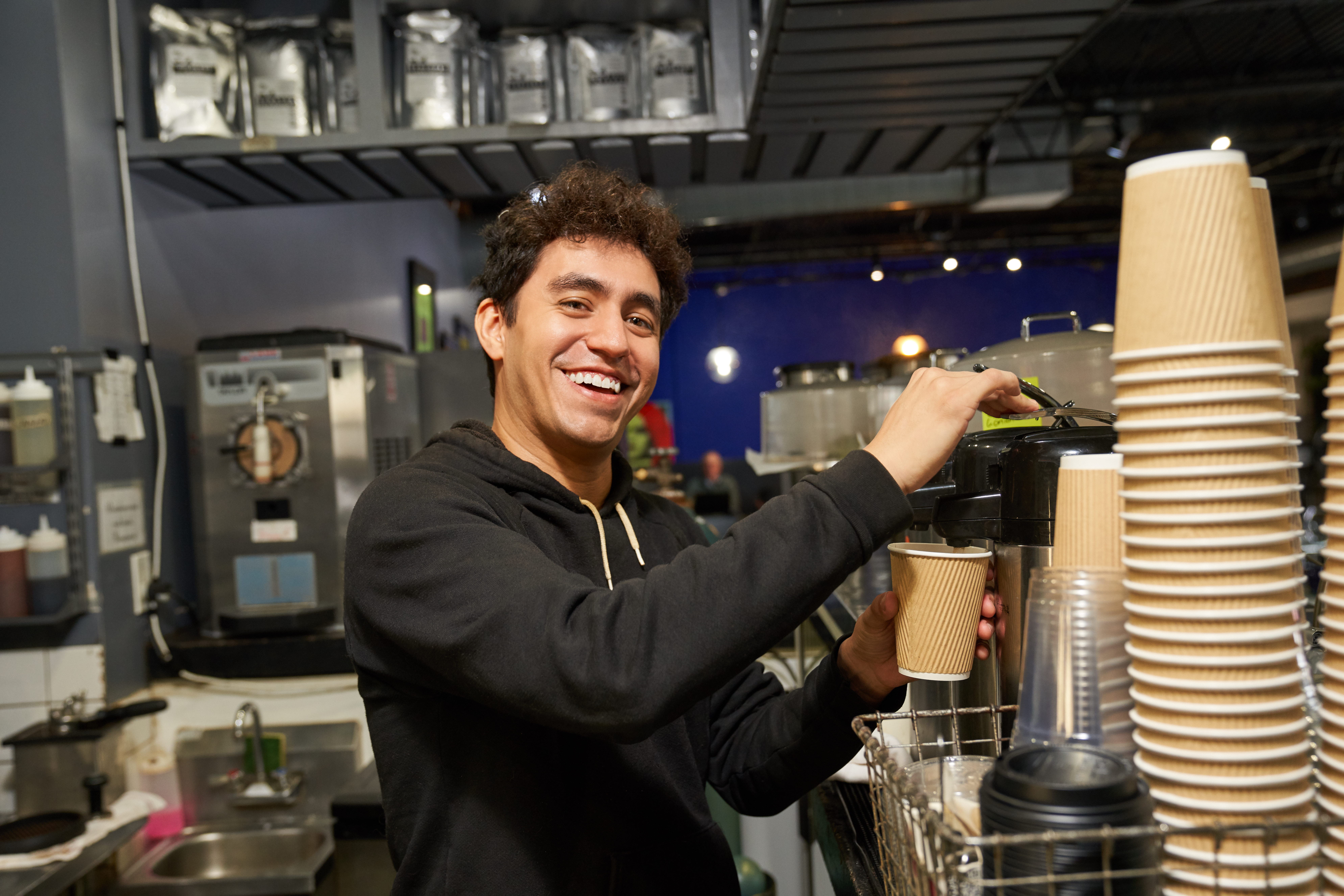 Man making coffee in coffee shop and smiling at camera